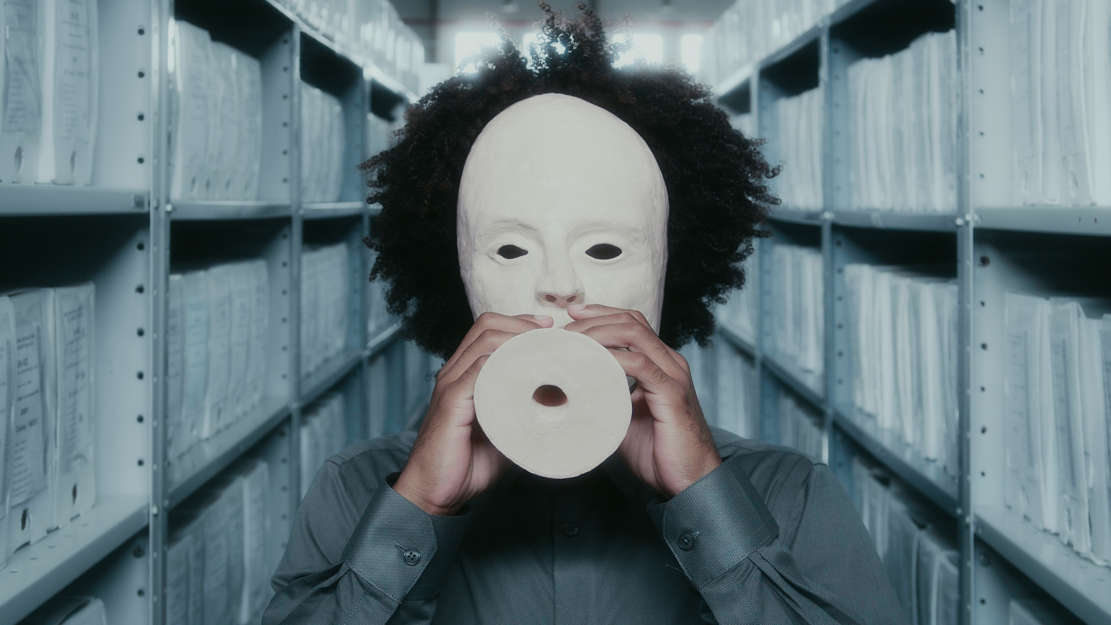 homem negro com uma máscara branca de cerâmica coreografando em um arquivo